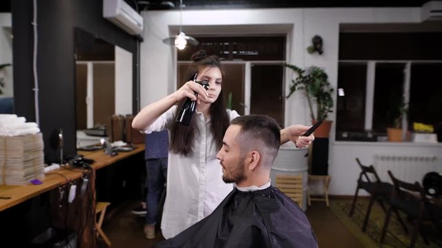 Man hipster visiting barber shop. Woman barber making stylish haircut. View of interior of barber shop