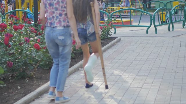 Mom helps my daughter with a broken leg on crutches to walk along the street