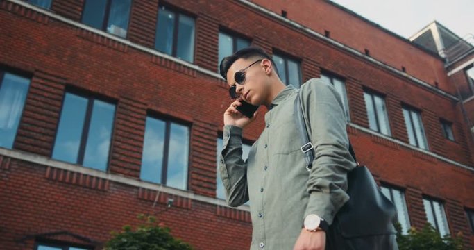 Handsome stylish young boy fashion casual clothes trendy sunglasses talking mobile phone city walking outdoors clock watch confidence house modern student side view below look fancy elegance street