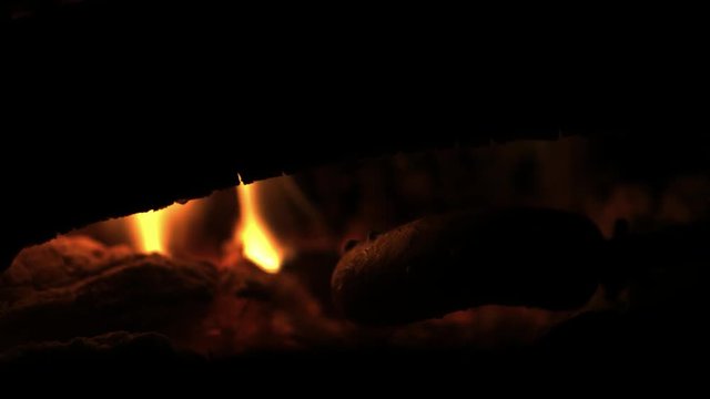 Making and cooking Hot dog sausages over open camp fire. Grilling food over flames of bonfire on wooden branch - stick spears in nature at night.