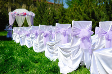Decor and decoration of the wedding ceremony with lilac or purple. Guest chairs with bows on the wedding arch background