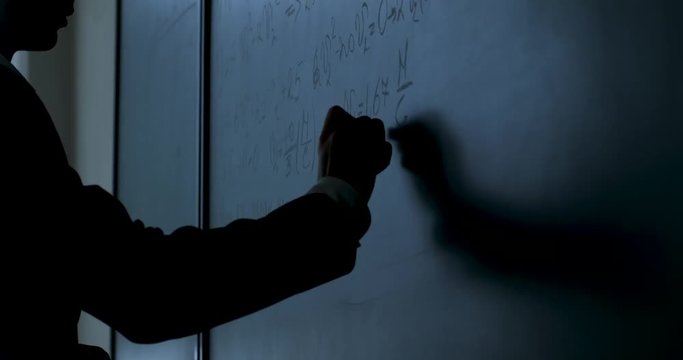 Scientist writing formulas on chalkboard. Hand with chalk wrote physics formulas on black chalkboard closeup