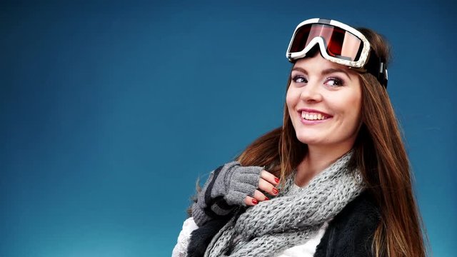 Woman smiling skier girl wearing warm clothing ski goggles portrait. Winter sport activity. Beautiful long hair sportswoman on blue studio shot, full HD
