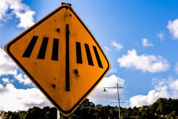 Sign: Pedestrian Crossing, yellow. Blue cloudy sky and trees in background