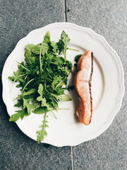 Salmon and arugula rucolla salad dish on white plate 