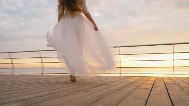 Beautiful bride in long white dress running on wooden embankment to sea or ocean. Slow motion.