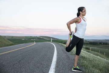 a young athletic woman stretching on the side of a paved road