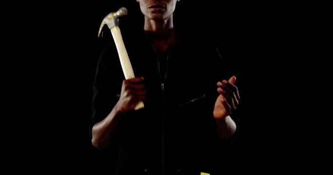 Androgynous man posing with hammer against black background