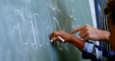 Teacher assisting schoolboy in writing alphabet on chalkboard - Powered by Adobe