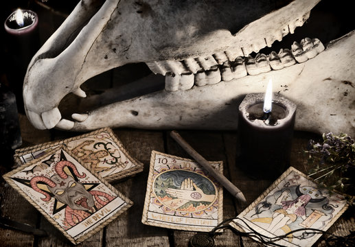 Scary skull with the Tarot cards, herbs, pencil and black candles. Mystic Halloween still life 