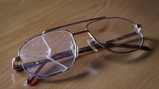 A Pair of broken eyeglasses is set down on a table