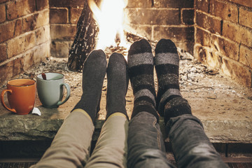 Couple in wool socks warming by cozy fire.