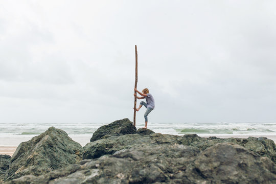 Wild marooned man standing on rocks holding a piece of driftwood
