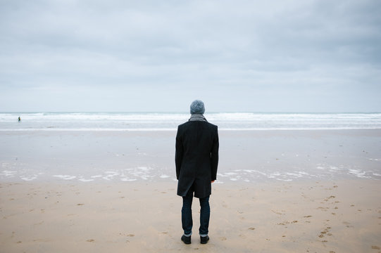 Man standing on a beach watching a surfer