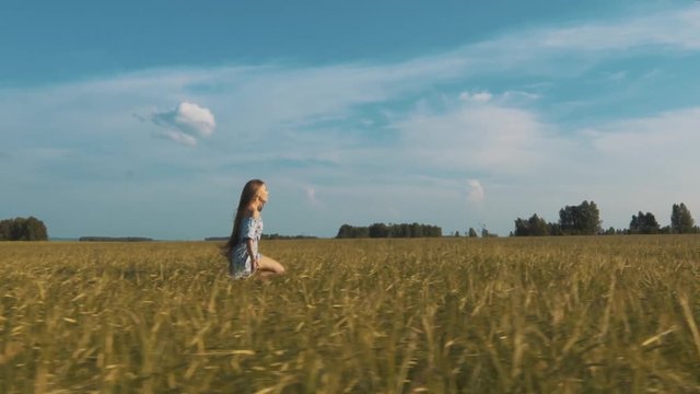 Beautiful young woman running across the wheat field looking around.