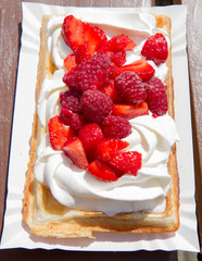 Waffle topped with whipped cream and freshly chopped strawberries and raspberries on a paper plate