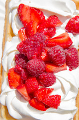 Waffle topped with whipped cream and freshly chopped strawberries and raspberries on a paper plate
