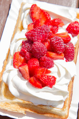 Waffle topped with whipped cream and freshly chopped strawberries and raspberries on a paper plate