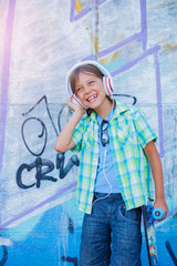 Cute boy with skateboard outdoors, standing on the street with different colorful graffiti on the walls