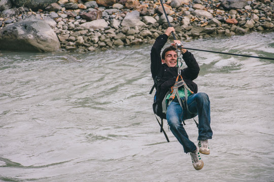 Young man on a canopy or zipline crossing a river on adventure travel