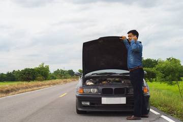 Man talking on a smartphone when broken car on the road.