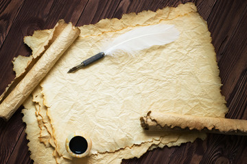 paper scroll with feather pen and ink pot on wood background
