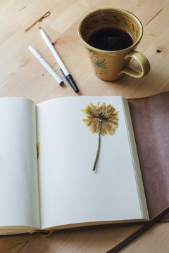 A blank journal lies open on a table next to a cup of coffee, a pen and an e-cigarette.