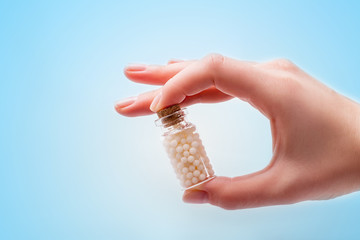 Woman hands holding a bottle with homeopathic pills on white background