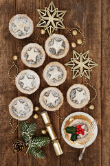 Traditional christmas mince pies with icing sugar dusting, holly, fir and gold bauble decorations on oak wood background.