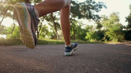 Girl runs through the park in the morning. Sporty young attractive brunette woman running on empty road in the morning. Slow motion. Only legs. - Powered by Adobe
