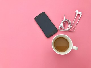 Closeup A black smartphone with A white earphone and a white cup of hot coffee set on pink background. The concept of morning activity. Top view with Copy space. Selective focus.