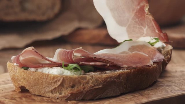Slow motion of italian speck put on rustic bread with arugula and ricotta cheese