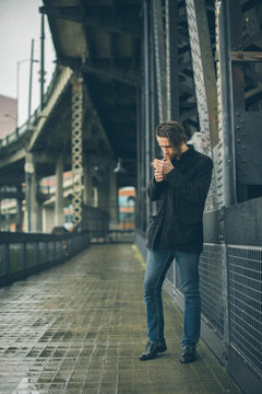 Man in Black Coat Lighting Cigarette on Industrial Metal Bridge