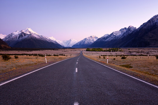 A straight highway leading to the snow capped mountains.