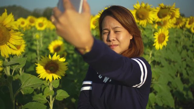 Beautiful girl in the sunflowers field takes a selfie phone share your photos online:Concept for family holiday.