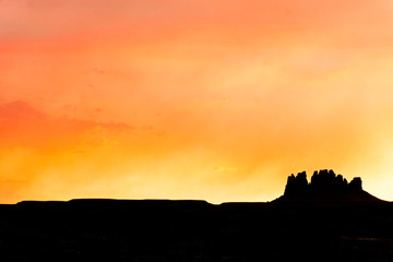 single mesa or rock formation in silhouette against a beautiful red and orange evening sky
