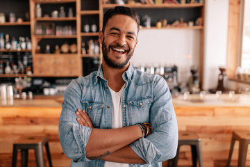 Happy young man standing with his arms crossed in a cafe