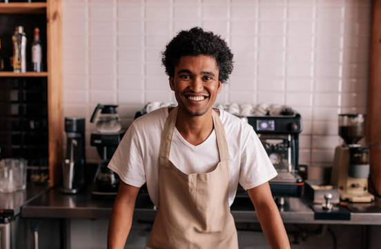 Happy young barista standing at cafe counter