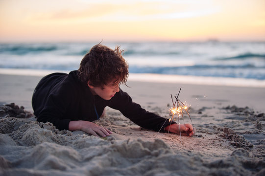 Boy playing with firework sparklers at the beach at sundown