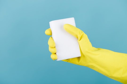 hand  in yellow glove holding sponge on blue background. cleaning
