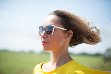 Beautiful blond young woman in yellow dress and glasses, hair develop in the wind