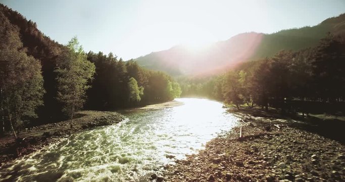 4k (UHD) aerial view. Low flight over fresh cold mountain river at sunny summer morning. Green trees and sun rays.