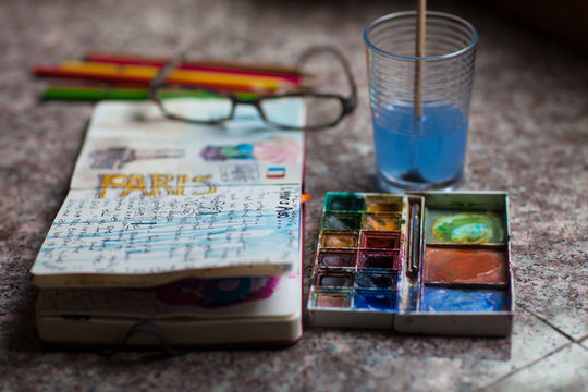 Journal open to a page about Paris with paint and pencils