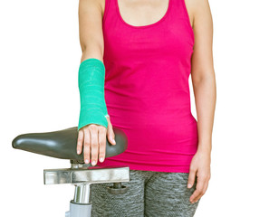 Injury woman wearing sportswear with green cast on hand and arm touching exercise bike at home, body injury concept