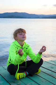 девочка на причале медитирует на фоне зари 