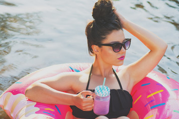 Young woman in pink donut float in pool or river relaxing holding cold drink