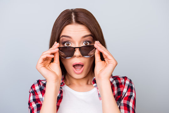 Cute amazed brunette girl tourist in shirt, holding her trendy glasses, she is shocked, with wide open eyes and mouth on pure background