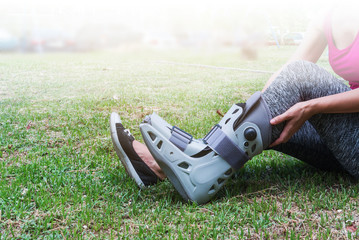 injured woman wearing sportswear  broken ankle wearing ankle support on exercise equipment in a public park background, health care concept