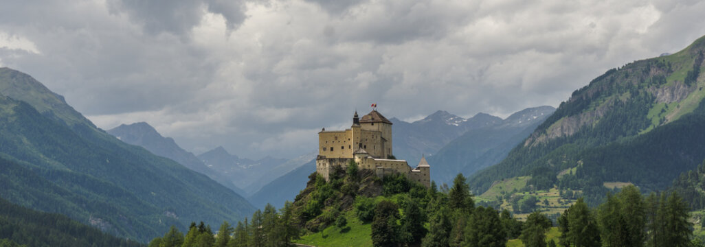 panoramic view of the lower Engadin valley and a medieval castle on a hill in the Swiss Alps underneath a cloudy sky