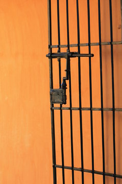 Close-up architectural detail of a traditional Spanish wrought iron gate featuring vertical decorative bars, an old-fashioned metal latch, warm terracotta-orange wall. Mediterranean architectural